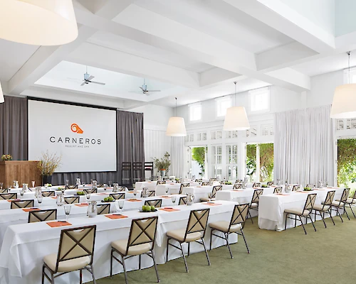 A bright conference room set up with tables, chairs, a large screen displaying 